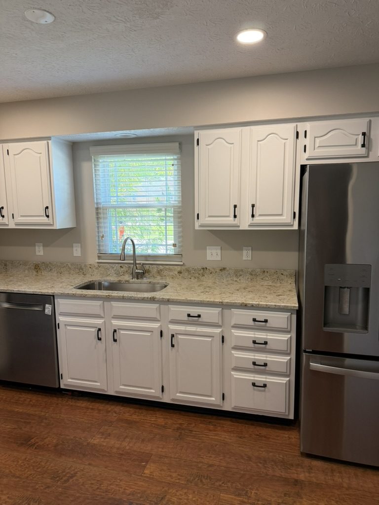 Oak cabinets refinished white with black pulls along a kitchen sink wall