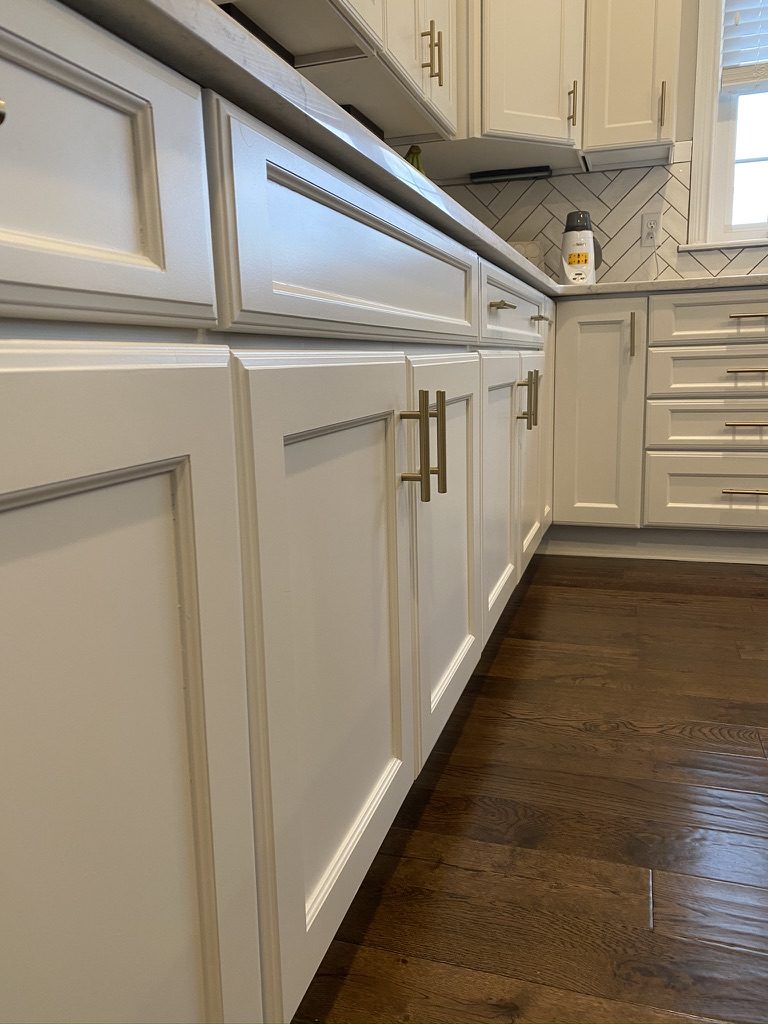 White painted lower cabinets with gold bar pulls and herringbone backsplash
